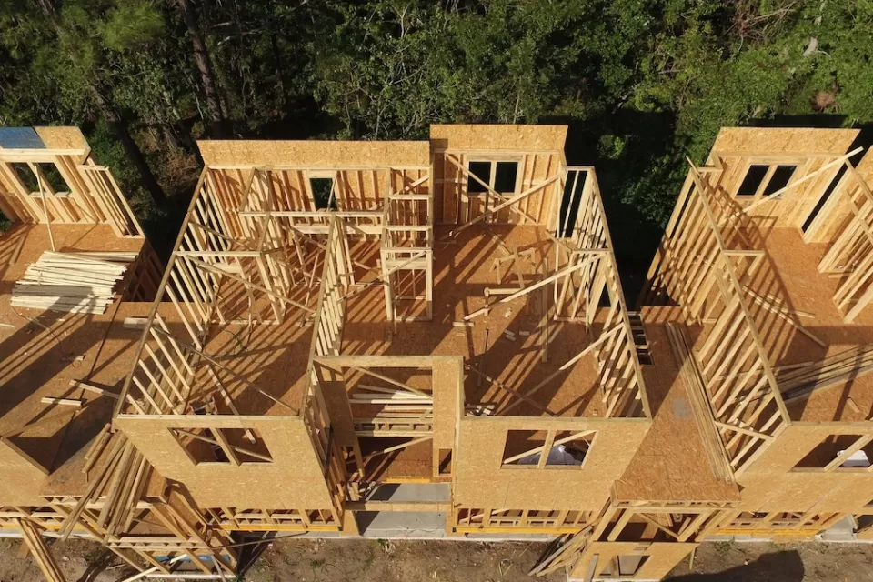 View from above of wood-frame multifamily housing under construction next to green trees.
